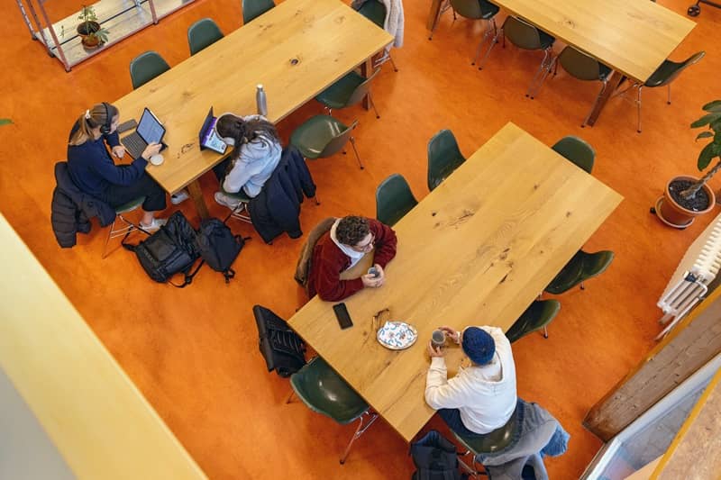 An langen Holztischen sitzen Studenten und trinken Kaffee oder arbeiten an Laptops